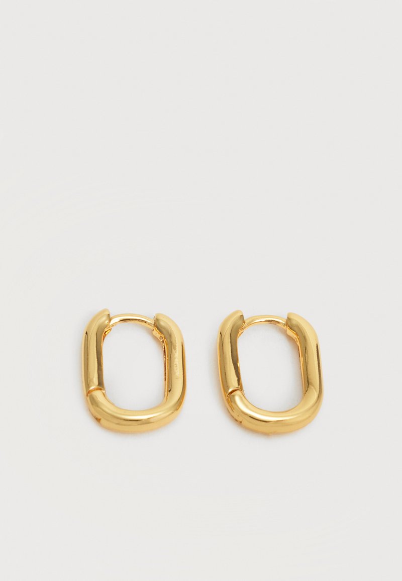 Ζευγάρι μικρών, χοντρών χρυσών οβάλ κρίκων σκουλαρικιών με λείο, γυαλιστερό φινίρισμα σε απλό φωτεινό φόντο.
