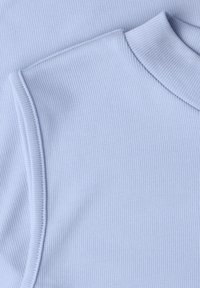Gros plan sur un tissu côtelé bleu clair montrant un haut sans manches avec un col rond haut et des coutures détaillées.