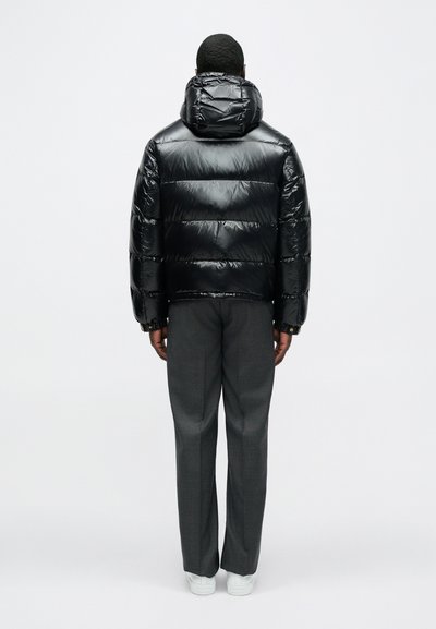 Sort dunjakke med en blank finish og hætte, med quiltede sektioner. Kombineret med grå skræddersyede bukser og hvide sneakers.