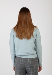 Maglione azzurro chiaro realizzato in un materiale morbido, con decorazioni sparse. Abbinato a pantaloni grigi a quadri, che mostrano una vestibilità sartoriale.