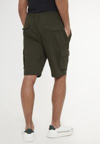 Pantaloni cargo verde oliva con vita elasticizzata, tasche laterali e posteriori, e vestibilità rilassata. Indossati con sneakers bianche.