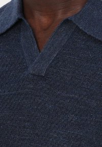 Laivastonsininen neulepusero, jossa on V-pääntie ja teksturoitu kangas. Kaulus on litteä ja hieman kohotettu, ja siinä on hieno kiilto sekä pehmeä viimeistely.