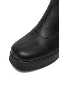 Czarny skórzany botek z zaokrągloną czubkiem, charakteryzujący się gładką teksturą, delikatnymi detalami przeszyć oraz grubą, platformową podeszwą.