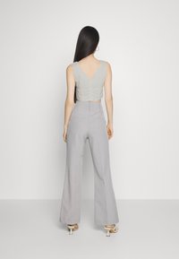 Svetlošedý cropped top s V-zadným výstrihom, skombinovaný s vysokými a širokými šedými nohavicami. Hladká textúra a minimalistický dizajn.