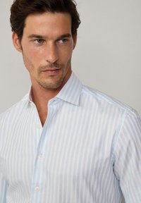 Camicia a righe blu chiaro e bianca con colletto button-down, caratterizzata da una texture liscia e una leggera lucentezza. Due bottoni visibili.