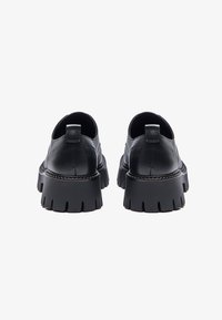 Chaussures en cuir noir avec une semelle épaisse. Forme arrondie, texture lisse et un discret tirette à l'arrière. Semelle épaisse avec des crans pour une adhérence accrue.
