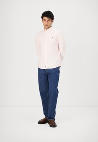 Lichtroze button-up overhemd met een klein logo, gecombineerd met donkerblauwe denim jeans en bruine schoenen. Casual fit, gladde stofstructuur.