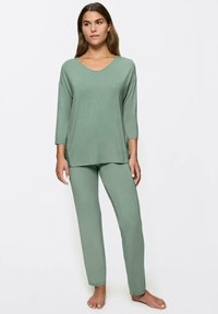 Conjunto de ropa de estar en verde claro que incluye una camiseta de corte holgado con escote en V y manga 3/4, junto con pantalones ajustados a juego. Textura suave y lisa.