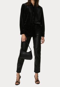 Czarna aksamitna koszula na guziki, czarne spodnie z imitacji skóry, czarna mini torebka oraz czarne sandały na cienkich paskach. Gładka faktura, dopasowany krój.