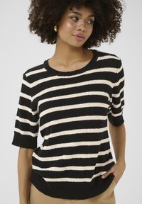 Pull en tricot à rayures noires et crème avec des manches courtes et un col rond. Tissu texturé avec une coupe décontractée. L'ourlet présente une légère courbe.