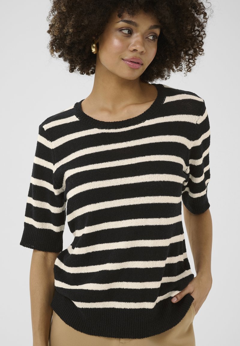 Pull en tricot à rayures noires et crème avec des manches courtes et un col rond. Tissu texturé avec une coupe décontractée. L'ourlet présente une légère courbe.