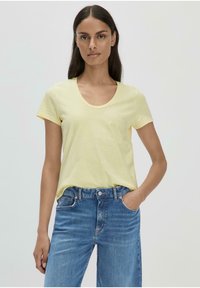 Gelbes T-Shirt mit kurzen Ärmeln, Rundhalsausschnitt und lässiger Passform, kombiniert mit blauen Jeans aus Denim. Der Stoff wirkt weich und leicht.