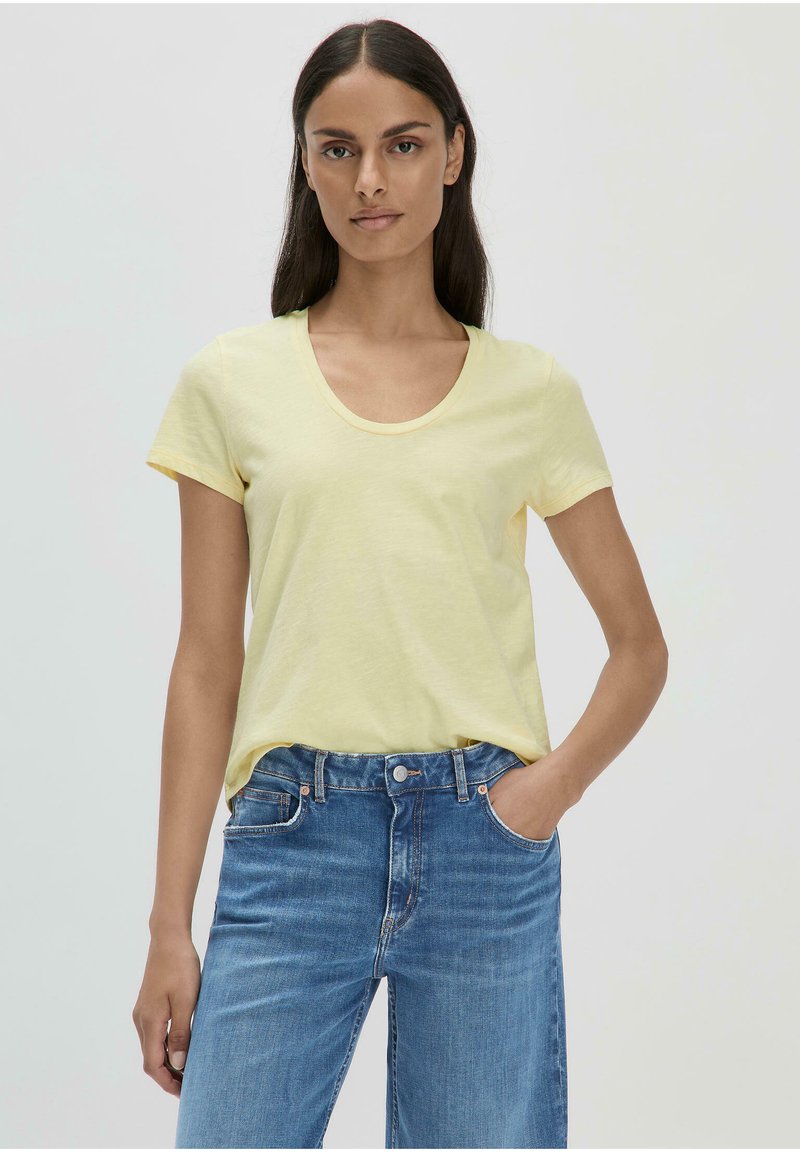 Gelbes T-Shirt mit kurzen Ärmeln, Rundhalsausschnitt und lässiger Passform, kombiniert mit blauen Jeans aus Denim. Der Stoff wirkt weich und leicht.