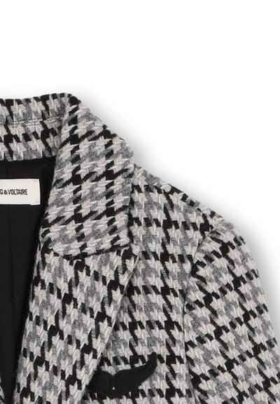 Veste tissée en motif pied-de-poule gris et noir, avec un accent en feutre noir en forme de moustache sur la poche gauche et un col cranté.