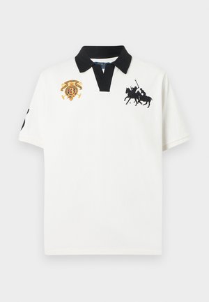 Bijela polo majica kratkih rukava s crnim ovratnikom, crnim logotipom igrača polo na desnoj strani prsa i izvezenim šarenim grbom na lijevoj strani prsa.