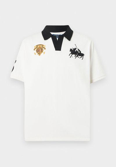 Λευκό πόλο μπλουζάκι με κοντά μανίκια, μαύρο γιακά, μαύρο λογότυπο παίκτη πόλο στο δεξί στήθος και κεντημένο πολύχρωμο έμβλημα στο αριστερό στήθος.