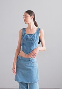 Top scurt din denim, cu decolteu pătrat și corp potrivit. Asortat cu o fustă mini din denim. Culoare albastru deschis, textură netedă.