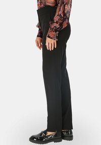 Czarne spodnie o kroju prostym, z bocznymi kieszeniami i gładką fakturą. W zestawieniu z błyszczącymi czarnymi mokasynami dla uzyskania kontrastu.