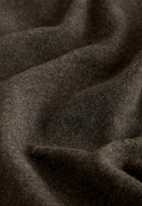 Hnedá vlnená tkanina s mäkkým, textúrovaným povrchom; prevesená s viditeľnými záhybmi a variáciami odtieňov, čím vytvára bohatý, teplý vzhľad.