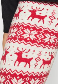 Red and white knitted leggings featuring a reindeer and snowflake pattern, with a textured finish and zigzag accents along the hem.