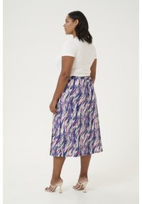 Jupe maxi présentant un motif ondulé bleu, rose et blanc, fabriquée en tissu léger. Associée à un t-shirt blanc ajusté et des talons crème.