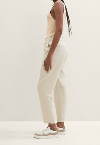 Beige ribbad linne, vita vida byxor med elastisk midja, kombinerat med vita och bruna sneakers, visat från en sida.