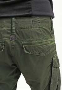 Gröna cargobyxor i ett texturerat bomullsmaterial, med flera fickor och sömdetaljer. Midjan är enkel utan utsmyckningar.