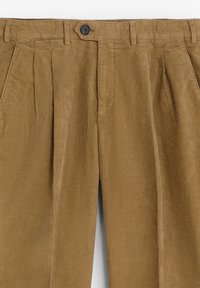 Pantalones de pana en un cálido color marrón, con un diseño plisado, un cierre de botón único y bolsillos laterales. Tejido texturizado con estrías verticales.