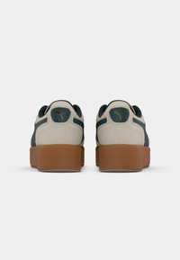 Sneakers with a beige suede upper, green accents, and a brown rubber outsole. PUMA logo in gold on the back and sides. Rounded shape.