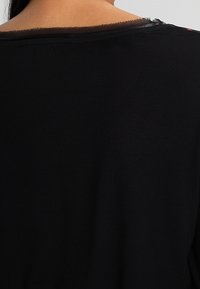 Schwarzes Kurzarmoberteil mit Rundhalsausschnitt, das einen rohen Saum und einen leicht lockeren Sitz aufweist. Glatte Textur mit leichtem Glanz.