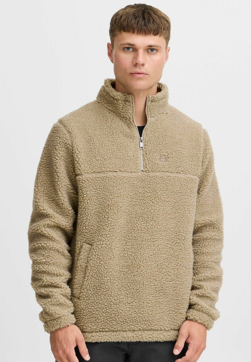 Beiger Fleece-Pullover mit hohem Kragen, halbmirtelbarem Reißverschluss und strukturiertem Material. Verfügt über seitliche Taschen und elastische Bündchen.