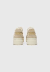 Beige zamšādas kurpes ar pūkainu krējuma krāsas oderi, ar paaugstinātu platformas zoli un iegravētu logotipu uz papēža. Tīrs un minimālists dizains.