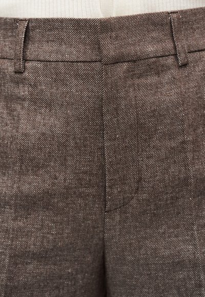 Gros plan sur un pantalon en tissu marron texturé avec passants de ceinture et fermeture avant dissimulée, associé à un haut tricoté blanc côtelé.