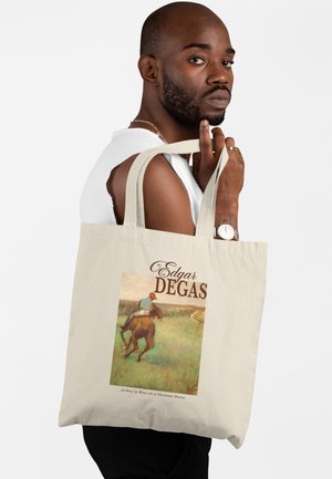 Uomo con canottiera bianca che porta una borsa tote beige con la riproduzione di un dipinto di Edgar Degas raffigurante un fantino su un cavallo.