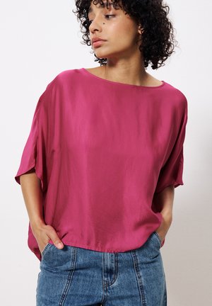 Fuchsia Seidenbluse mit kurzen Ärmeln und weitem Ausschnitt, kombiniert mit hochgeschnittenen Jeans aus Denim mit klassischem Fünf-Taschen-Design.