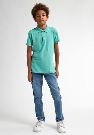 Tricou polo turcoaz cu accente verzi, cu două butoane, asortat cu blugi din denim albastru deschis și adidași albi, având un design simplu.