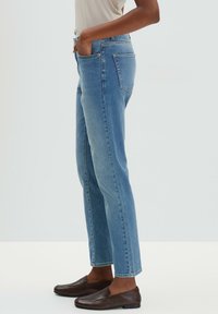 Jeans taille haute, bleu clair, à jambes droites avec cinq poches, passants de ceinture et ourlet brut. Texture en denim lisse et coupe régulière.