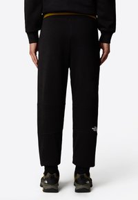 Czarne dresy o zwężającym się kroju, z elastycznym paskiem w talii i wyraźnym przeszyciem. Logo marki jest widoczne na dolnej części nogawki.