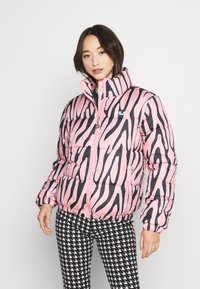 Giacca a vento con stampa zebra nera e rosa, colletto alto, chiusura con zip e polsini elasticizzati; abbinata a pantaloni a scacchi bianco e nero.