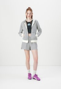 Hoodie rayé, shorts assortis, crop top noir avec logo, baskets violettes, chaussettes blanches. Tissu en mélange de coton, design décontracté.