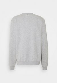 Sudadera gris con mangas largas, cuello redondo y puños acanalados. Presenta un pequeño logo verde en la parte posterior del cuello. Tejido suave y texturizado.