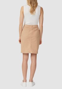 Lichtbeige denim rok met een getailleerde silhouet, middellang, twee achterzakken en een gladde textuur, gecombineerd met een wit geribbeld tanktop.
