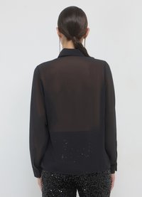 Blouse noire transparente à manches longues avec col, présentant une section inférieure ornée de sequins. Texture lisse, coupe ajustée et poignets boutonnés.