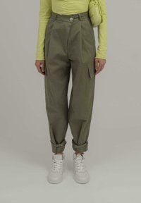 Olivengrønne cargo-bukser med rullede manchetter, udstyret med frontfolder og sidelommer, parret med hvide sneakers og en limegrøn top.