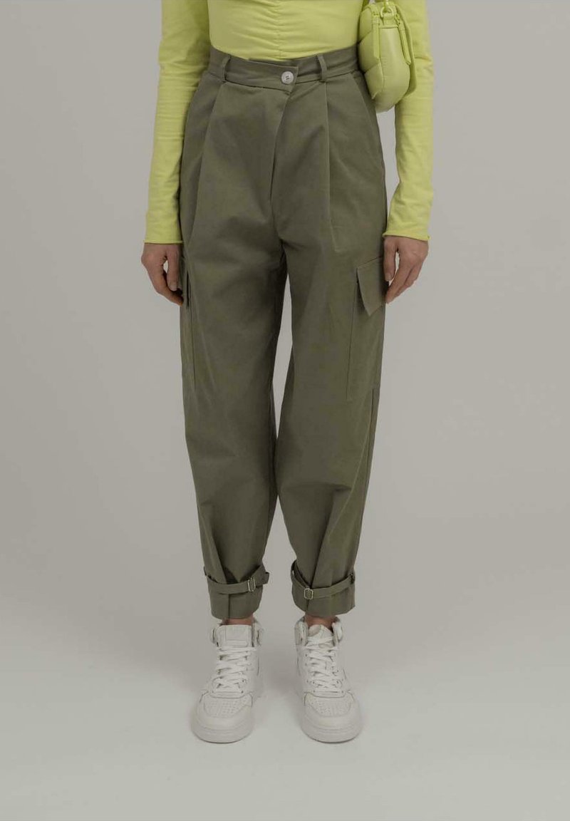 Olivengrønne cargo-bukser med rullede manchetter, udstyret med frontfolder og sidelommer, parret med hvide sneakers og en limegrøn top.