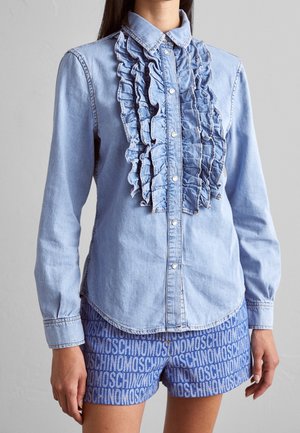 Chemise en denim bleu clair avec un détail froncé sur le devant, fermeture à boutons et manches longues. Assortie avec un short bleu comportant un motif de logo répété.