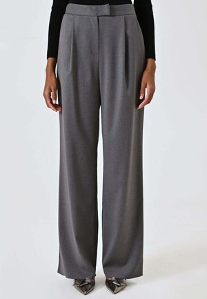 Pantaloni grigi su misura con vita alta, design a gamba larga e pieghe sul davanti, abbinati a scarpe metalliche con punta appuntita.