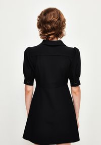 Vestido negro con un cuerpo ajustado, mangas cortas abullonadas y un cuello. Presenta una cintura ceñida y una falda acampanada. Textura de tela suave.