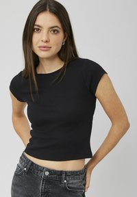 T-shirt noir court en maille côtelée avec des manches courtes, présentant un col rond. Le tissu a une finition texturée, associé à un jean foncé taille haute.