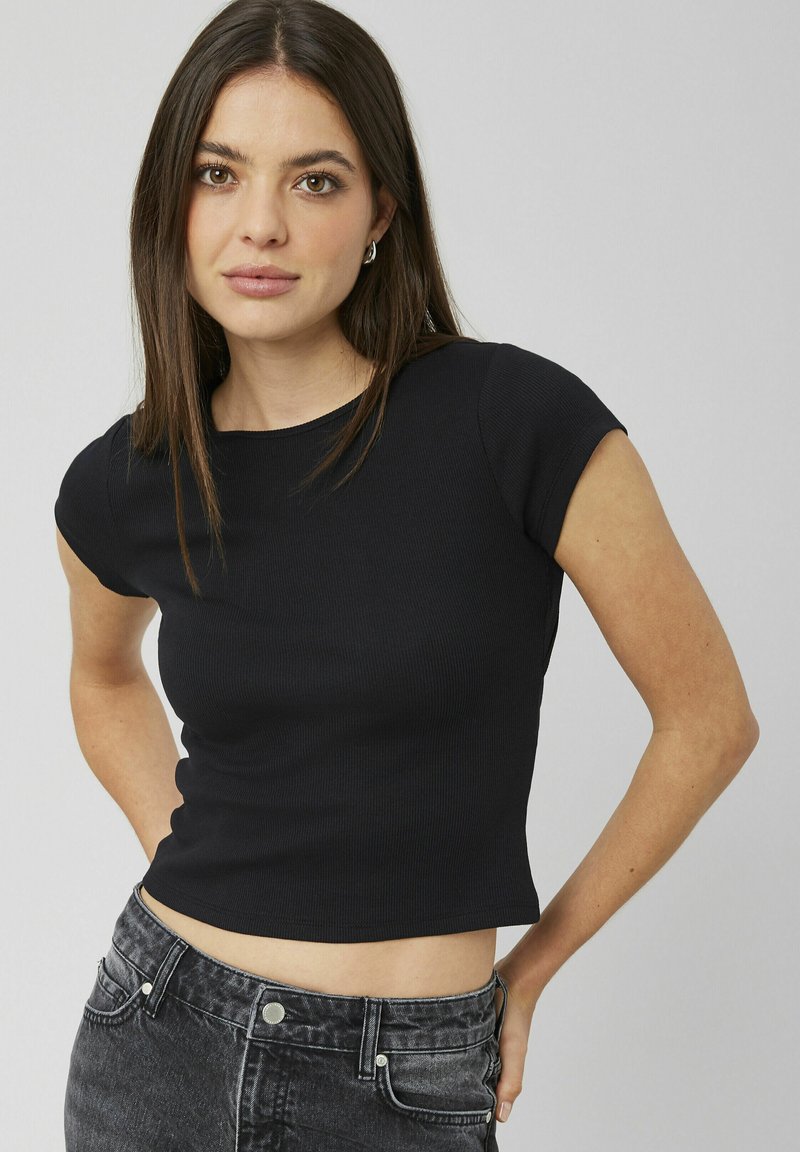 T-shirt noir court en maille côtelée avec des manches courtes, présentant un col rond. Le tissu a une finition texturée, associé à un jean foncé taille haute.